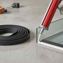 Coiled black EPDM rubber seal profile beside silicone sealant being applied to a glazing joint with a caulking gun